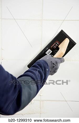 Stock Image - Laying tiles, glue mortar, using grout float, new homes under construction, construction site. Fotosearch