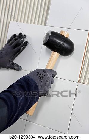 Laying tiles on glue mortar-covered wall using rubber mallet, new homes under construction, construction site View Large Photo Image Picture - Laying tiles on glue mortar-covered wall using rubber mallet, new homes under construction, construction site. Fotosearch