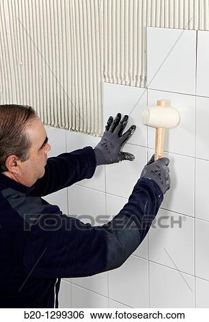 Laying tiles on glue mortar-covered wall using rubber mallet, new homes under construction, construction site View Large Photo Image Stock Photograph - Laying tiles on glue mortar-covered wall using rubber mallet, new homes under construction, construction site. Fotosearch