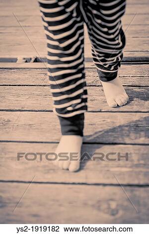 Stock Image - Legs and feet of baby girl walking barefooted on wooden jetty. Fotosearch