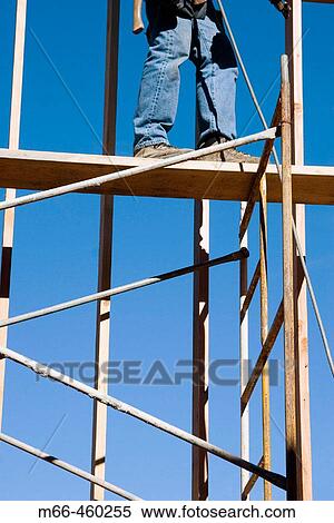 Stock Photography - Legs of carpenter standing atop scaffolding at a construction site.. Fotosearch