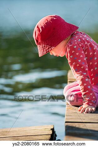 Lifestyle moment of summer childhood. Little girl sitting on jetty, looking down. View Large Photo Image Stock Photography - Lifestyle moment of summer childhood. Little girl sitting on jetty, looking down.. Fotosearch