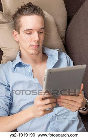 Stock Image - Lifestyle moment with a relaxed young adult male holding a digital tablet device in his hands. Fotosearch