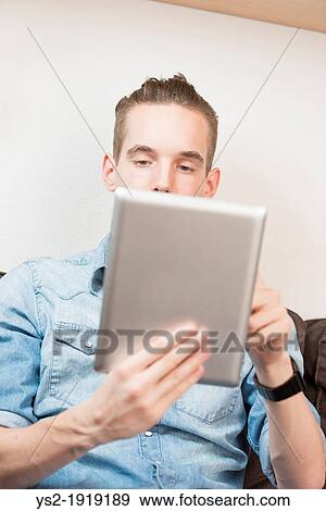 Stock Photo - Lifestyle moment with a relaxed young adult male holding a digital tablet device in his hands. Fotosearch