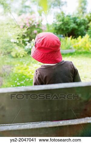 Stock Image - Lifestyle moment with young girl watching a garden filled with flowers and green plants.. Fotosearch