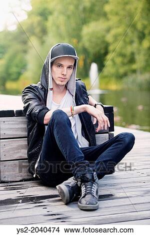 Lifestyle portrait of young man in leather jacket sitting in a park looking at camera. View Large Photo Image Picture - Lifestyle portrait of young man in leather jacket sitting in a park looking at camera.. Fotosearch