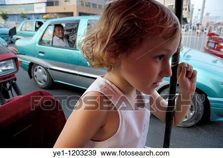 Little blond girl inside a red motor tricycle speeding along a busy boulevard in Datong, Shanxi, China. View Large Photo Image Stock Photo - Little blond girl inside a red motor tricycle speeding along a busy boulevard in Datong, Shanxi, China.. Fotosearch