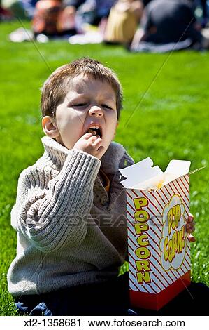 Little boy sitting in a grassy park eating popcorn View Large Photo Image Stock Image - Little boy sitting in a grassy park eating popcorn. Fotosearch