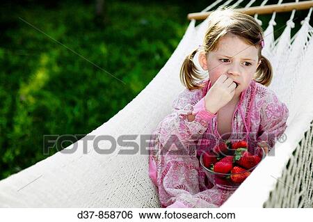 Stock Photograph - Little girl eating strawberries in the garden. Fotosearch