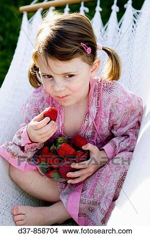Picture - Little girl eating strawberries on a hammock. Fotosearch
