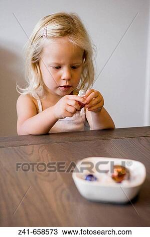 Little girl peeling a bonbon View Large Photo Image Stock Image - Little girl peeling a bonbon. Fotosearch