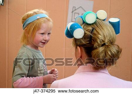Stock Photography - Little girl pretending to be a hairdresser, putting rollers in teachers hair. Fotosearch