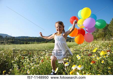 Stock Image - Little girl running with coloured balloons through a spring meadow. Fotosearch