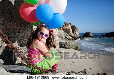 little girl sitting at the ocean with balloons, looking at the camera View Large Photo Image Stock Photo - little girl sitting at the ocean with balloons, looking at the camera. Fotosearch