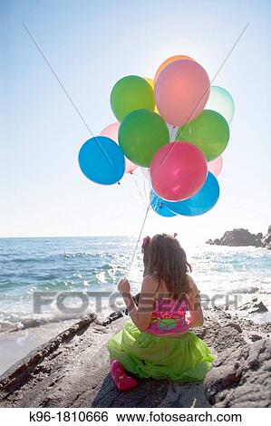 little girl sitting on rocks, holding balloons, overlooking the ocean View Large Photo Image Stock Photograph - little girl sitting on rocks, holding balloons, overlooking the ocean. Fotosearch