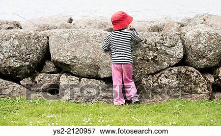 Little girl standing alone by big stones watching the sea. View Large Photo Image Stock Photo - Little girl standing alone by big stones watching the sea.. Fotosearch