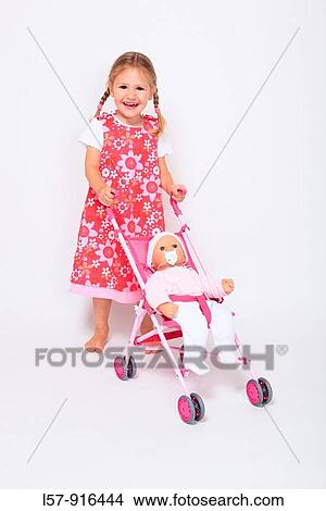 Picture - little girl wearing dress standing with buggy pram and baby doll, white background, studio, Switzerland. Fotosearch