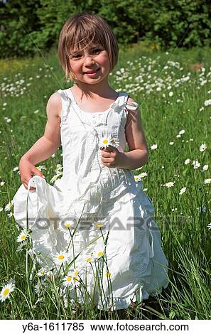 Little girl wearing white dress standing in field holding daisies smiling portrait View Large Photo Image Stock Photography - Little girl wearing white dress standing in field holding daisies smiling portrait. Fotosearch