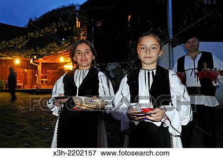 Stock Photo - little girls in traditional costume wellcoming the visitors at a restaurant with locals in the village of Sibiel, department of Sibiu, Transylvania, Romania, Southeastern and Central Europe.. Fotosearch