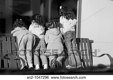 Little girls standing on a public bench View Large Photo Image Stock Photograph - Little girls standing on a public bench. Fotosearch