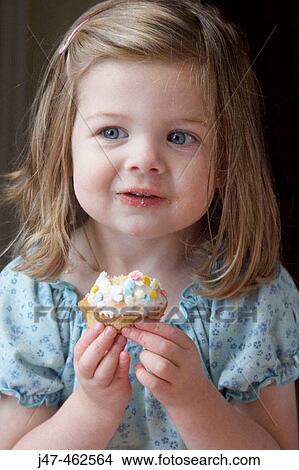 Little girl's third birthday party, eating a bun, smiling View Large Photo Image Picture - Little girl's third birthday party, eating a bun, smiling. Fotosearch