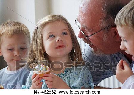 Little girls third birthday party, eating a bun, smiling, with her grandad. View Large Photo Image Stock Image - Little girls third birthday party, eating a bun, smiling, with her grandad.. Fotosearch
