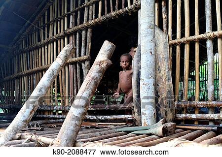 Stock Photo - Little man standing a the entrance to a traditional house, Papua, Indonesia, Southeast Asia.. Fotosearch