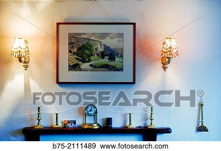 Stock Photo - Living room of a house with a fire place and a painting hunging on the wall and lights on. Yorkshire Dales, England, UK, Europe.. Fotosearch