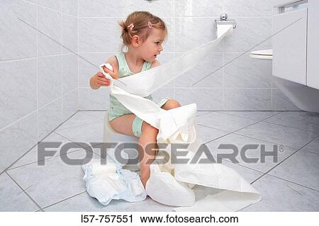 Stock Image - Llittle girl sitting on Potty in bathroom, unrolling toilette paper while doing potty training, playing and fooling around. Fotosearch