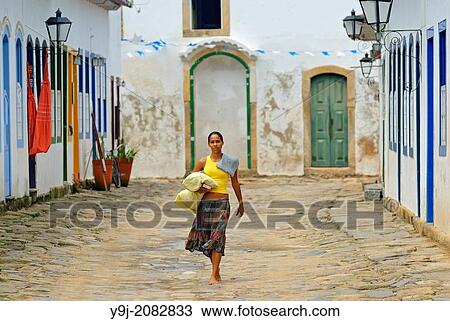 Stock Image - Local brazilian woman walking through the historic center; Paraty, Espirito Santo, Brazil. The beautiful colonial town of Paraty has been a UNESCO World Heritage Site since 1958.. Fotosearch