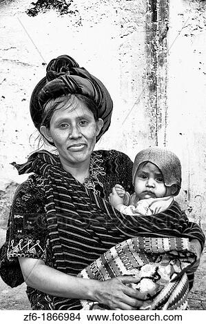 Local colorful woman against bright wall with local print dress carrying her baby in tourist village of Antigua Guatemala View Large Photo Image Picture - Local colorful woman against bright wall with local print dress carrying her baby in tourist village of Antigua Guatemala. Fotosearch