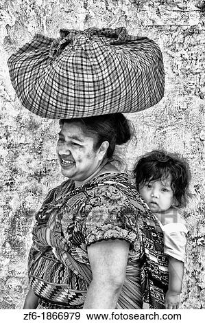 Local colorful woman against bright wall with local print dress carrying her baby on back in tourist village of Antigua Guatemala View Large Photo Image Stock Photo - Local colorful woman against bright wall with local print dress carrying her baby on back in tourist village of Antigua Guatemala. Fotosearch