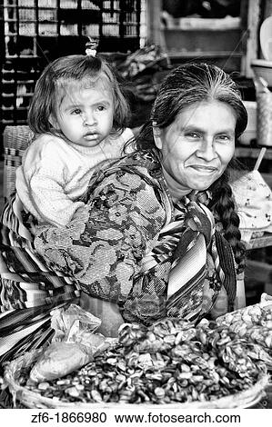 Stock Image - Local colorful woman with grand daughter on back in market in tourist village of Antigua Guatemala. Fotosearch