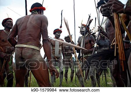 Picture - Local group of nacked Papuas showing a playful fight in traditional headdress and with weapons, Jayawijaya region, Papua, Indonesia, Southeast Asia. Fotosearch