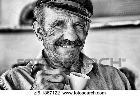 Stock Image - Local man portrait with Greek coffee with Greek hat at restuarant in white in Mykonos in Greek Islands in Greece Europe. Fotosearch