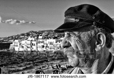 Local portait of man in Greek hat scene of downtown near beach with famous white buildings of Little Venice in Mykonos in the Greek Islands in Greece Europe View Large Photo Image Stock Photo - Local portait of man in Greek hat scene of downtown near beach with famous white buildings of Little Venice in Mykonos in the Greek Islands in Greece Europe. Fotosearch