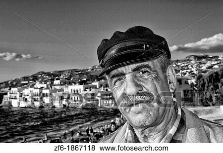 Local portait of man in Greek hat scene of downtown near beach with famous white buildings of Little Venice in Mykonos in the Greek Islands in Greece Europe View Large Photo Image Stock Photo - Local portait of man in Greek hat scene of downtown near beach with famous white buildings of Little Venice in Mykonos in the Greek Islands in Greece Europe. Fotosearch