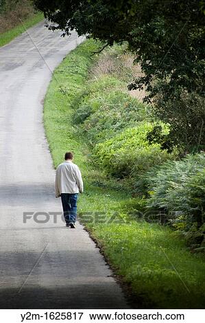 Stock Photo - Lone man walking along a road Green, nature, solitude. Fotosearch