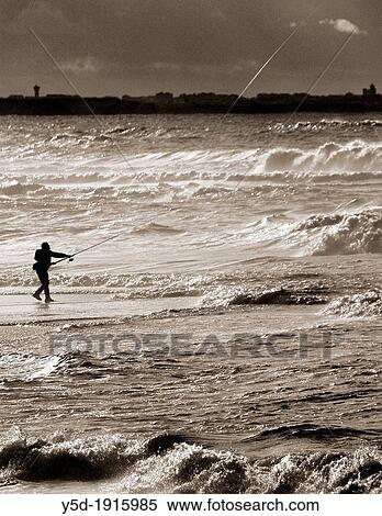 Stock Photography - lonely fisherman fishing with a rod directly from Atlantic Ocean, at dusk, Foz do Arelho is a little town on Atlantic Ocean coast and with beautiful Obidos Lagoon, Silver Coast, Portugal. Fotosearch