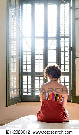 Lonely woman sitting on a bed looking at the window. View Large Photo Image Stock Image - Lonely woman sitting on a bed looking at the window.. Fotosearch