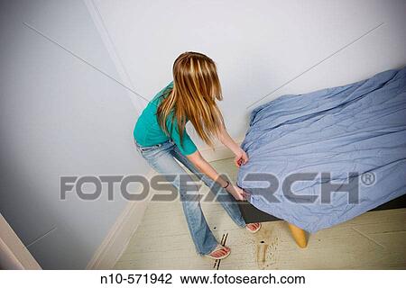 Stock Image - Long blond-hair teen girl putting a sheet onto a bed. Fotosearch