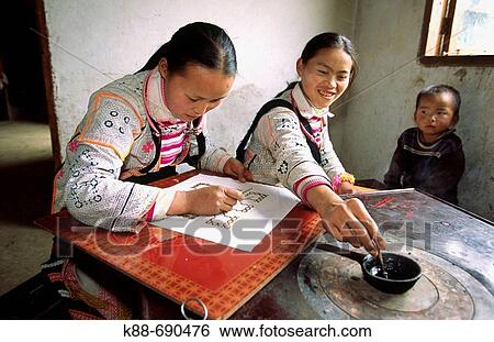 Stock Photograph - Long horn miao girls using batik technique to decorate textile used for traditional clothing, Guizhou, China. Fotosearch