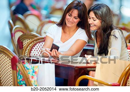 Picture - Looking a smartphone. Women sisters 35 and 40 years taking coffee on a terrace. Donostia. San Sebastian. Gipuzkoa. Basque Country- Spain.. Fotosearch