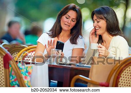 Picture - Looking a smartphone. Women sisters 35 and 40 years taking coffee on a terrace. Donostia. San Sebastian. Gipuzkoa. Basque Country- Spain.. Fotosearch