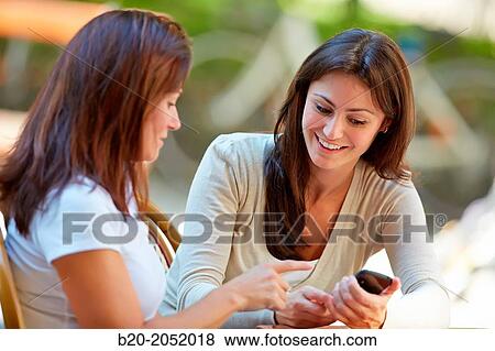 Stock Photo - Looking a smartphone. Women sisters 35 and 40 years taking coffee on a terrace. Donostia. San Sebastian. Gipuzkoa. Basque Country- Spain.. Fotosearch