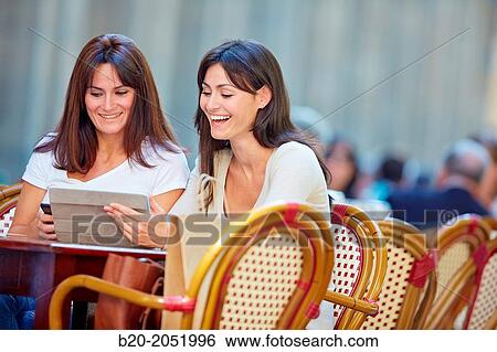 Stock Photograph - Looking a tablet. Women sisters 35 and 40 years taking coffee on a terrace. Donostia. San Sebastian. Gipuzkoa. Basque Country- Spain.. Fotosearch