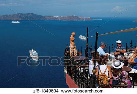 Picture - Looking down at restaurant and the sea with ships at harbor with statue in Santorini Greece in Greek Islands. Fotosearch