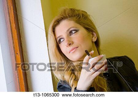 Stock Image - Looking outside with a cup of coffee in hand young woman portrait. Fotosearch