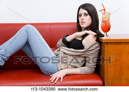 Stock Image - Lounging on a Red sofa with a cocktail attractive young woman. Fotosearch