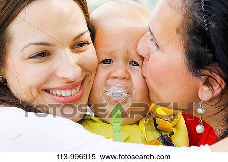 Stock Photography - Love is pain, one year old baby boy squeezed between two young ladies. Fotosearch